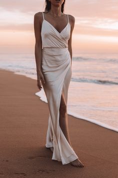 a woman standing on top of a beach next to the ocean wearing a white dress