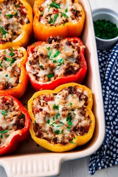 several stuffed peppers in a casserole dish with sauce and parsley on the side