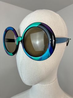 ERA - 1960s  LABEL - Emilio Pucci  TYPE - Sunglasses COLOR - Multi     FEATURES - These sunglasses are so iconic and instantly recognizable! Features an abstract geometric Pucci print with blues, black, green, and purple. The sunglasses are a dramatic large oversized round shape with tinted lenses. Comes complete with a matching case. A great pair of designer shades from the 1960s. The ultimate vintage accessory piece. Made in France.                   MATERIAL - Plastic     CONDITION - Excellent condition - the lenses are in good shape with minimal scratches (the right lens has a longer hairline scratch not visible when wearing them)           MEASUREMENTS Frame length - 6.5" Frame height - 3" Temples are 6.5" apart at the widest part  All items are vintage and may show natural signs of w Retro Round Frame Glass Sunglasses, Retro Round Sunglasses With Gradient Lenses, Vintage Round Frame Sunglasses For Party, Retro Polarized Sunglasses For Party, Retro Glass Sunglasses For Parties, Retro Glass Sunglasses For Party, Mid-century Sunglasses With Tinted Lenses For Summer, Retro Round Sunglasses With Uv Protection, Retro Party Sunglasses With Glass Lenses