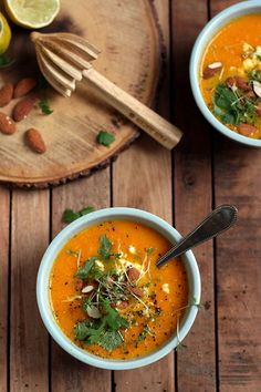 two bowls of carrot soup with garnishes and nuts on a wooden table