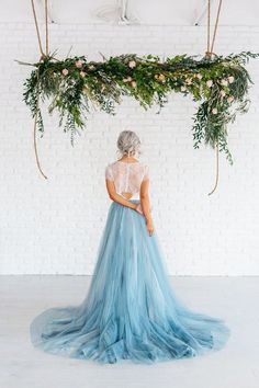 a woman in a blue dress is standing under a floral arch with greenery on it