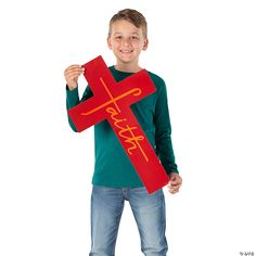 a young boy holding up a red cross with the word jesus written on it and smiling