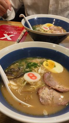 two bowls of soup with meat, noodles and eggs on the side at a restaurant