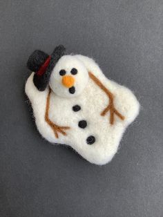 a small felt snowman with a hat and scarf on it's head, sitting on a gray surface