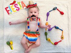 a baby wearing a hat and tie laying on top of a towel next to toys