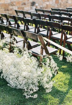 rows of wooden chairs with white flowers in the grass next to each other at an outdoor ceremony