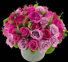 a bouquet of pink and purple roses in a white vase on a black background with greenery