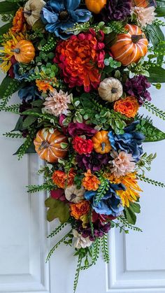 an orange and blue wreath is hanging on the front door with pumpkins, leaves and flowers