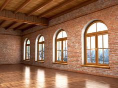 an empty room with three arched windows and wood flooring on one side, in front of a brick wall