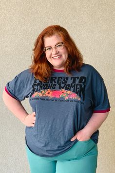 Natural Life tees are a great way to look cute and put positive sentiments out into the world. This graphic reads "Here's to strong women. May we know them. May we be them. May we raise them." Short-sleeve crewneck graphic tee with contrast bands on the neckline and sleeve openings for a retro look. Indigo blue-grey color with magenta contrasting bands. Black screen printed text with colorful flowers in orange, fuchsia, green and purple. 60% Cotton / 40% Polyester Crewneck Graphic, Women Graphic, Black Screen, Judy Blue Jeans, Natural Life, Oversized Silhouette, Retro Look, Indigo Blue, Grey Color