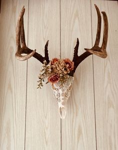 a deer's head with antlers and flowers in it on a wooden floor