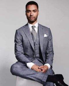 a man in a suit and tie sitting on a chair with his legs crossed, looking at the camera