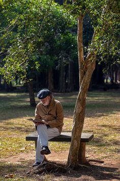 a man sitting on a bench next to a tree and looking at his cell phone