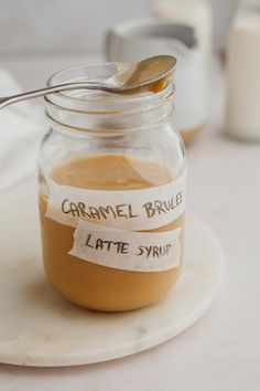 a spoon sitting in a glass jar filled with caramel sauce on top of a white plate