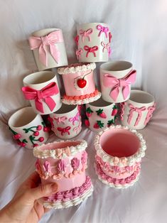 a hand holding a pink and white cake in front of many cupcakes with bows on them