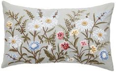 an embroidered pillow with daisies and other flowers on the front, in light grey