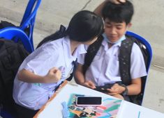 two young children sitting at a table looking at their cell phones