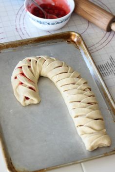 a pastry shaped like a worm sitting on top of a cookie sheet next to a bowl of jelly