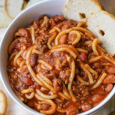 a white bowl filled with spaghetti and meat on top of a table next to bread