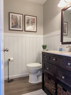 a white toilet sitting in a bathroom next to a wooden sink vanity and framed pictures on the wall