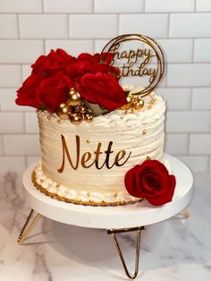 a white cake with red roses on top and happy birthday written on the side in gold lettering