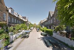 an empty street lined with houses next to trees and bushes on either side of the road