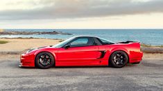 the red sports car is parked on the side of the road near the water and rocks