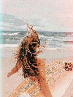 a woman sitting on top of a beach holding a surfboard next to the ocean