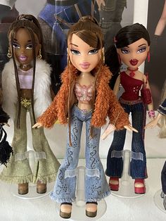 several dolls are lined up in front of a wall with pictures on it and one doll has her hair pulled back