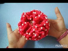 someone is holding up a red crocheted brooch with white pearls on it