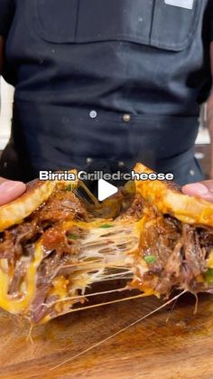 a person holding a sandwich with meat and cheese on it in front of a wooden cutting board