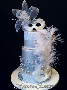 a three tiered cake decorated with white feathers and masks on it's side