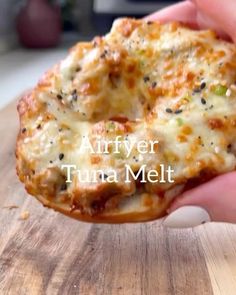 a person holding up a pizza with cheese and toppings on it that says air fryer tuna melt