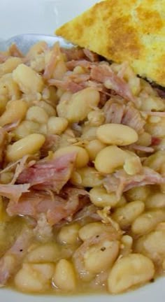 a white plate topped with beans and ham next to a piece of bread on top of a table