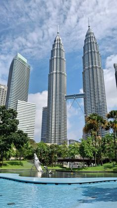 two large skyscrapers towering over a pool in the middle of a lush green park