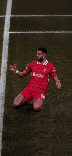 a soccer player sitting on the ground with his arms out and legs spread wide in front of him