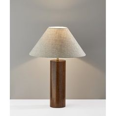 a wooden table lamp with a white shade on the base and a grey wall behind it