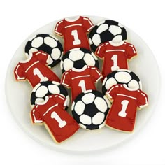 cookies decorated like soccer jerseys and balls on a white plate with the number one in red