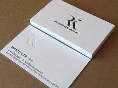 two white business cards sitting on top of a brown table with the letter k on it