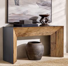 a vase sitting on top of a wooden table in front of a painting and artwork