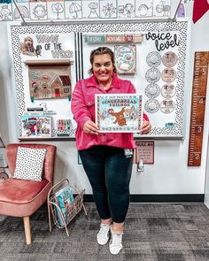 a woman holding up a book in front of a bulletin board