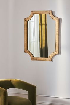 a mirror hanging on the wall next to a green chair in front of a white wall