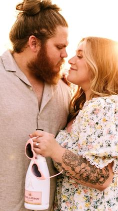 a man and woman embracing each other while holding a bottle with the sun behind them