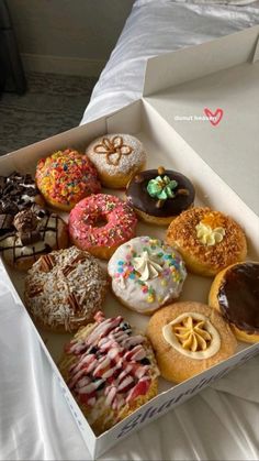 a box filled with lots of different flavored donuts on top of a bed