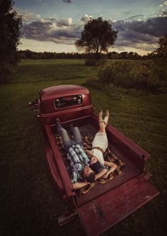 two people laying in the back of a red pickup truck with an open bed on it