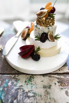 a white plate topped with a cake covered in cheese and fruit next to utensils