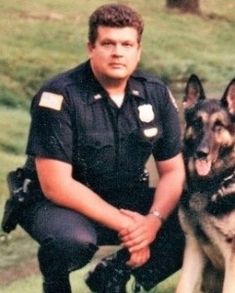 a police officer kneeling down next to a german shepard dog in front of a grassy field