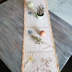 a table runner with flowers and eggs on it next to an egg cup, plant and vase