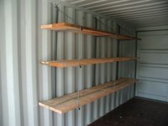 three wooden shelves are in the corner of a shipping container with metal bars hanging from them