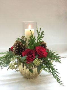 a vase filled with red roses and greenery next to a lit candle on a table